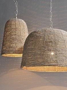 two woven lamps hanging from chains against a wall