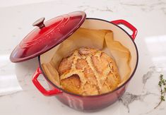 a red pot filled with bread on top of a white marble counter next to a sprig of rosemary