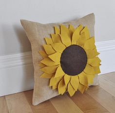 a pillow with a sunflower on it sitting on a wooden floor next to a wall