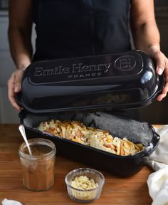 a person holding a pan filled with food on top of a wooden table next to a container