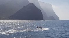 a small boat in the water near some mountains and cliffs on a clear day with sun reflecting off the water