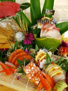 an assortment of sushi is displayed on a bamboo mat with green leaves and purple flowers