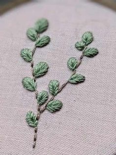 a close up of a piece of cloth with green leaves on it and thread in the middle