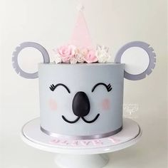 a birthday cake with a koala bear face and pink flowers on top, sitting on a pedestal