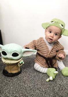 a baby in a crocheted hat sitting next to an infant yoda doll