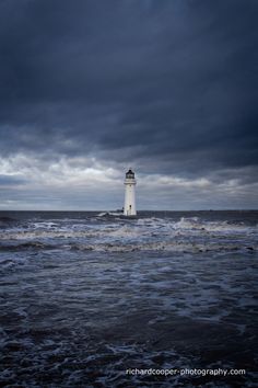 a light house in the middle of an ocean under a cloudy sky with dark clouds