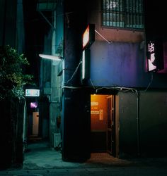 an alleyway at night with neon signs on the building's front and door