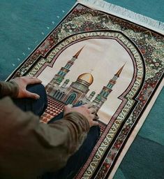 a person sitting on the floor with a rug in front of them that has an image of a mosque