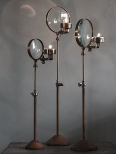 three antique brass lamps with mirrors on each one and two candles in the middle, against a white wall