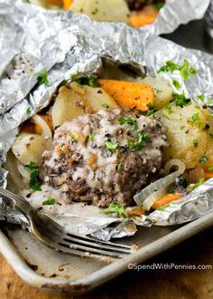 some food that is sitting in foil on a plate with a fork and spoon next to it