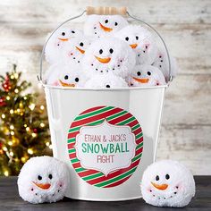 a red bucket filled with snowballs sitting on top of a table next to a christmas tree