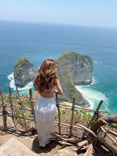 a woman standing at the top of a hill looking out over the ocean and cliffs