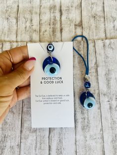 a hand holding a necklace with an evil eye on it and a card attached to it