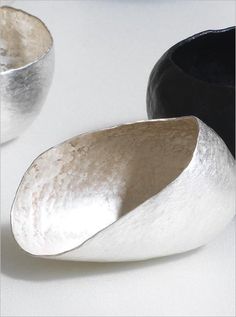 two silver and black bowls sitting on top of a white table next to each other