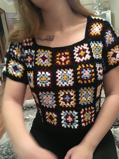 a woman is wearing a crocheted shirt and holding her hands in her pockets