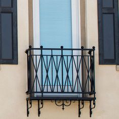 a balcony with black iron railing and blue shutters