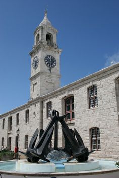 there is a clock tower in the background behind a fountain with sculptures on it's sides