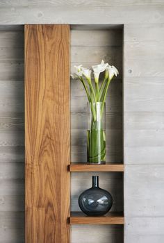 a vase with flowers in it sitting on a shelf next to a wooden paneled wall