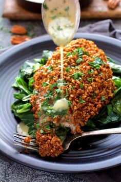 a piece of meat is being drizzled with sauce on top of greens