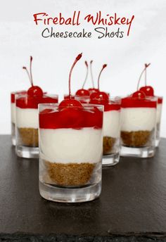 four small desserts with cherries and cheesecake shots on a black table top