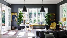 a living room filled with furniture and lots of windows covered in plants on top of them