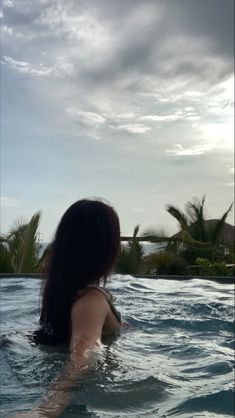 a woman sitting in the water with her back turned to the camera and looking at the sky