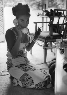 a woman sitting on the floor while talking on a phone and holding a telephone to her ear