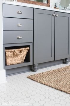 a bathroom with gray cabinets and white counter tops, rugs on the floor and a large mirror above it