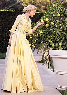 a woman in a long yellow dress standing next to a bush with fruit on it