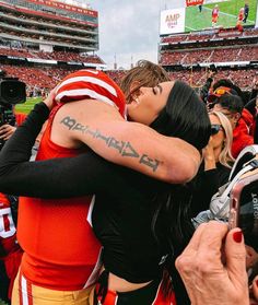 a football player is hugged by a woman at a game while fans take pictures on their cell phones