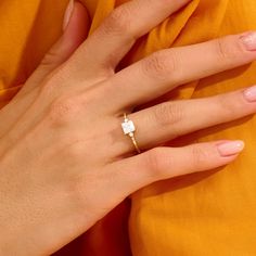 a woman's hand wearing a gold ring with a square shaped diamond on it