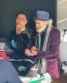 two men sitting next to each other in front of a blackboard with writing on it