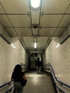 two people are walking up and down an escalator in a public building with white tiles on the walls