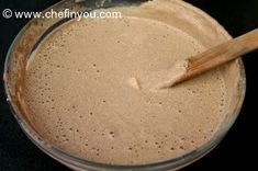 a glass bowl filled with brown liquid on top of a black counter next to a wooden spoon