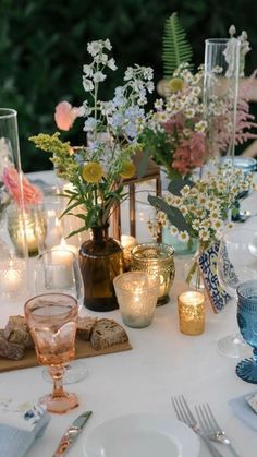 the table is set with flowers, candles and place settings for an outdoor dinner party