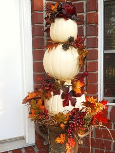 three white pumpkins are stacked on top of each other with autumn leaves around them