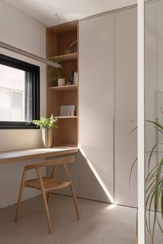 a room with a desk, bookshelf and plant in it next to a window