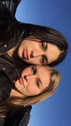 two young women standing next to each other in front of a blue sky and telephone pole