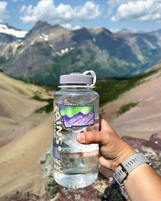 a hand holding a water bottle with mountains in the background