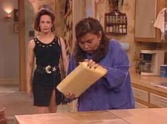 two women standing in a kitchen looking at something on the counter and one is holding a large container