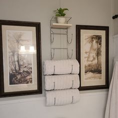 a bathroom with towels hanging on the wall and two pictures above the toilet in front of it