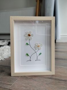 a white frame with flowers in it sitting on a wooden floor next to a rug