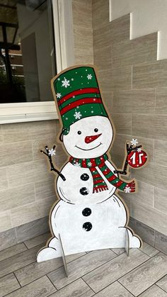 a cardboard snowman with a green hat and scarf holding a candy cane in his hand