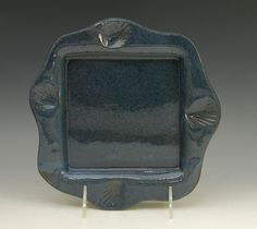 a blue square shaped dish with seashells on the rim and underglusted edges