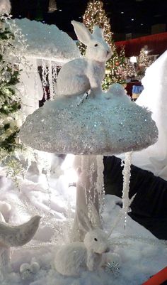 a display in a store filled with lots of fake snow and white rabbits sitting on top of a mushroom