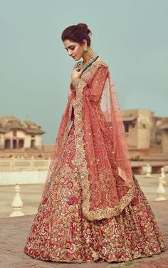 a woman in a red and gold bridal gown stands on a brick walkway, looking down at the ground