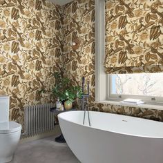 a white bath tub sitting next to a toilet in a bathroom under a window with roman shades