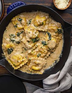 a skillet filled with chicken and spinach covered in gravy on top of a wooden table