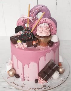 there is a pink cake with donuts and chocolates on it