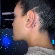 a woman with a small tattoo on her left side behind her ear, looking to the right